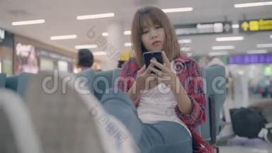 快乐的亚洲女人在机场登机口等待航班时，在候机大厅使用和检查她的智能手机。
